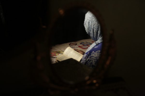 In this photo taken Tuesday April, 5. 2016 author Hadiza Nuhu Gudaji, is reflected in a mirror as she reads through one of her novels in Kano, Nigeria. In the local market stalls are signs of a feminist revolution with piles of poorly printed books by women, as part of a flourishing literary movement centered in the ancient city of Kano, that advocate against conservative Muslim traditions such as child marriage and quick divorces. (AP Photo/Sunday Alamba)