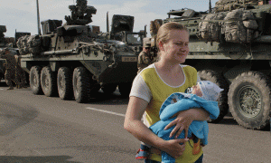 Një grua rumune me fëmijë në krah ecën pranë mjeteve të blinduara të ushtrisë amerikane në Ploiesti, Rumani më 13 maj 2015. (AP Photo/Vadim Ghirda)